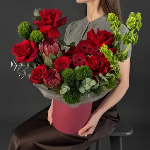 Цветочная композиция из красных роз, молюцеллы и протеи в шляпной коробке